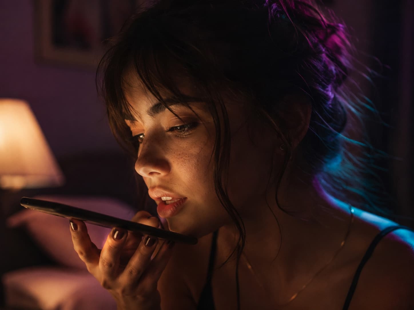 A phone screen glowing at night with a dreamy AI girlfriend portrait, dark blue neon bedroom atmosphere.